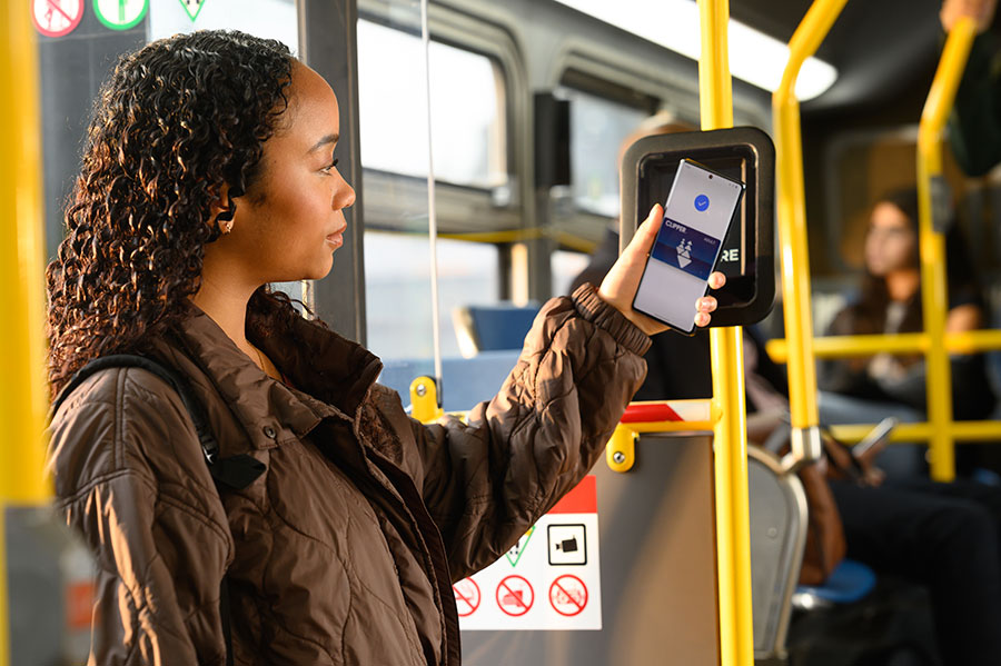 A youth boards a bus, holding up an Android phone to a Clipper card reader, with Clipper on their phone; a “Done” screen is displayed on the phone.