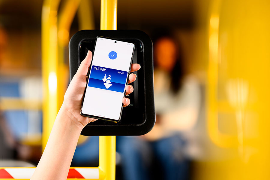 Close-up of a hand holding an Android up to the Clipper bus card reader, using Clipper on her phone to pay for transit; a “Done” screen is displayed on the phone.
