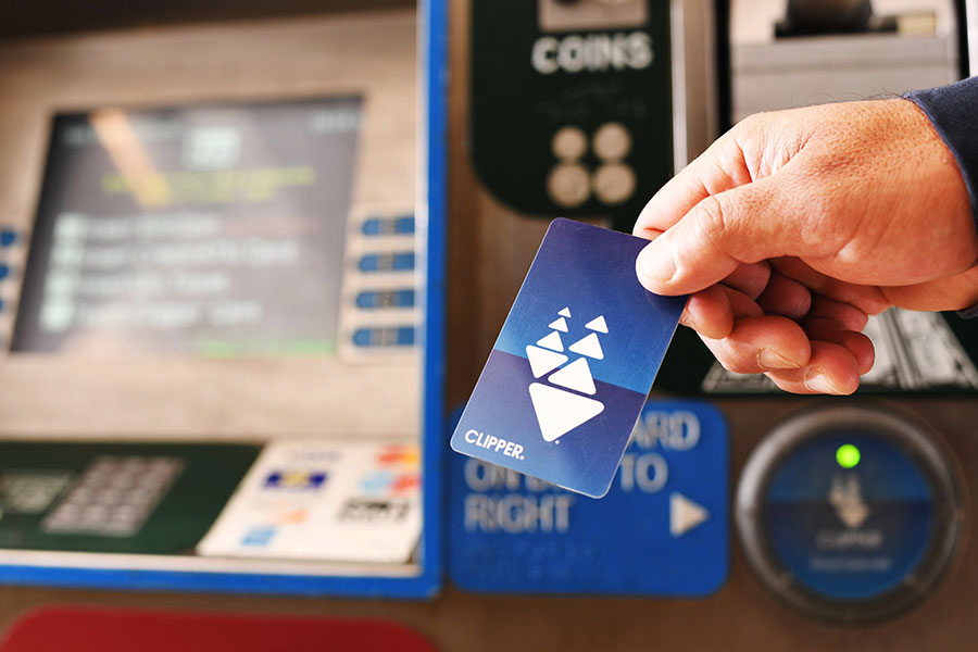 Close-up of a person's hand holding a plastic Clipper card in front of a BART ticket machine.