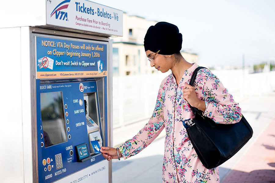 An adult standing in front of a VTA ticket machine, holding up their plastic Clipper card to add value.